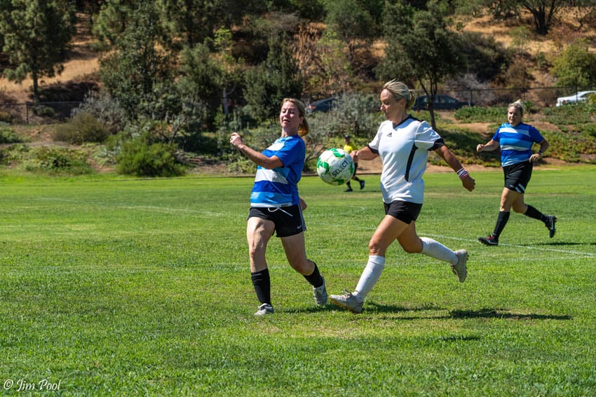 two female adult soccer opponents with ball in air during game