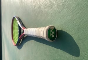 Yonex VCORE 100 tennis racket lying on tennis court semi blurred