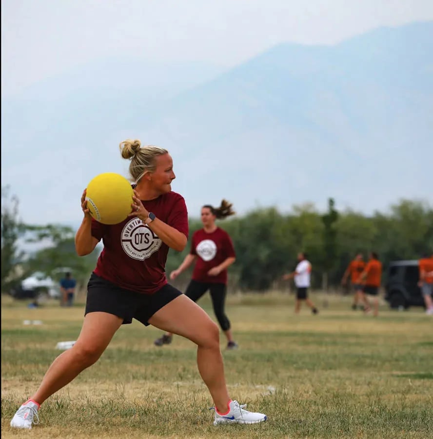 blonde woman holding yellow kickball getting ready to "pitch" it