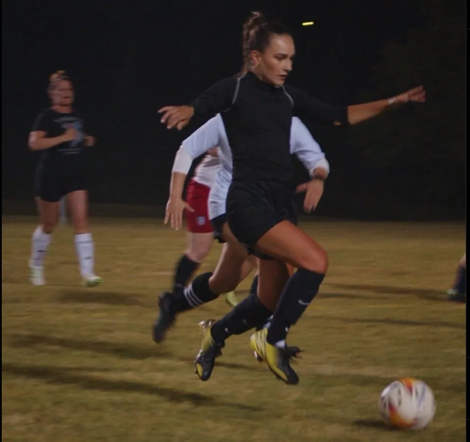 Adult female soccer players with one in foreground in black attacking ball