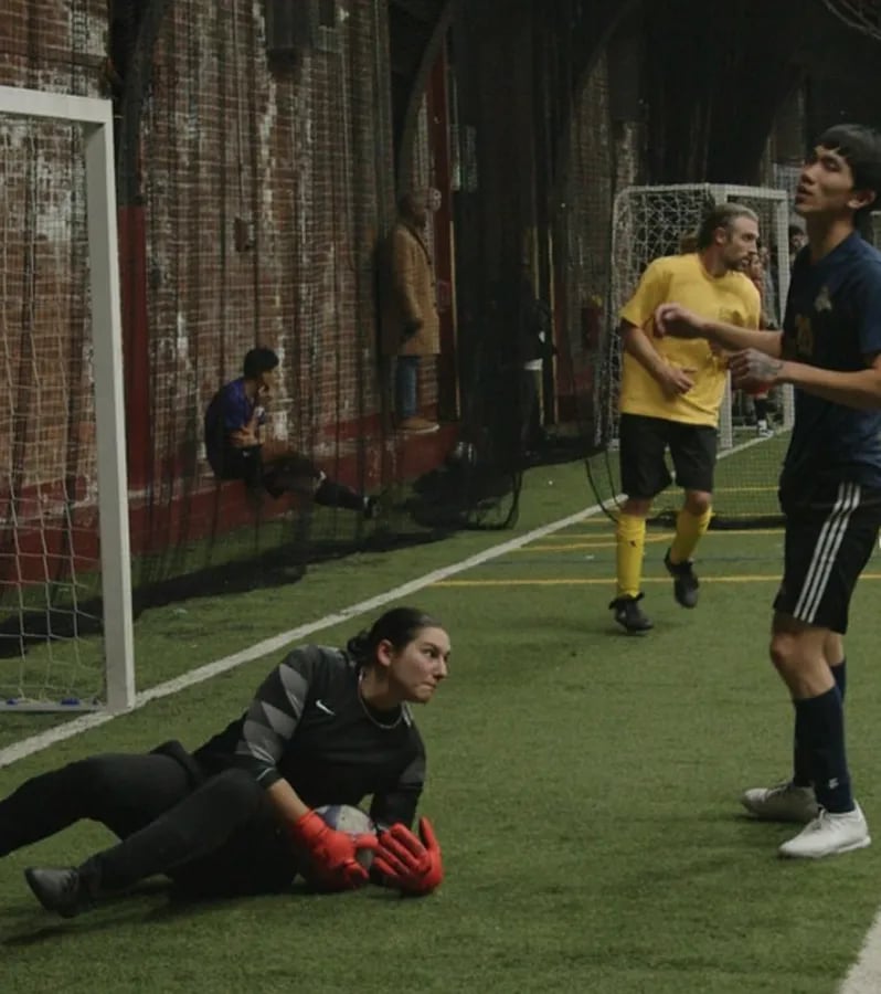 adult soccer co-ed indoor game with female goalie saving ball surrounded by two male players