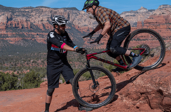 Man on mountain bike letting go of hands as instructor holds handlebars.