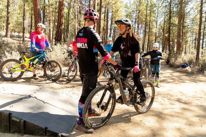 mountain bike instructor holding handlebars of student's bike as she stands upright on bike
