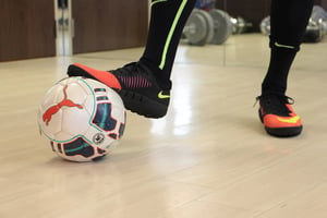 person in black futsal shoes with one foot on top of a soccer ball