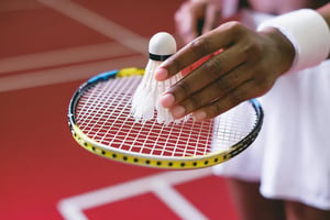 closeup-of-hand-holding-shuttlecock-atop-badminton-racquet.