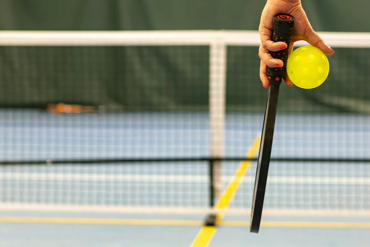 closeup of woman's hand holding pickleball and paddle