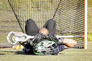 man lying down with lacrosse gear in front of goal