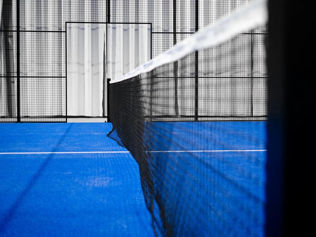 close up of net and blue padel court with walls