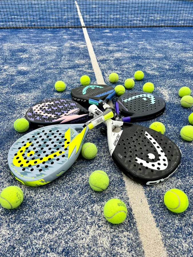 four padels and a bunch of yellow balls lying on court