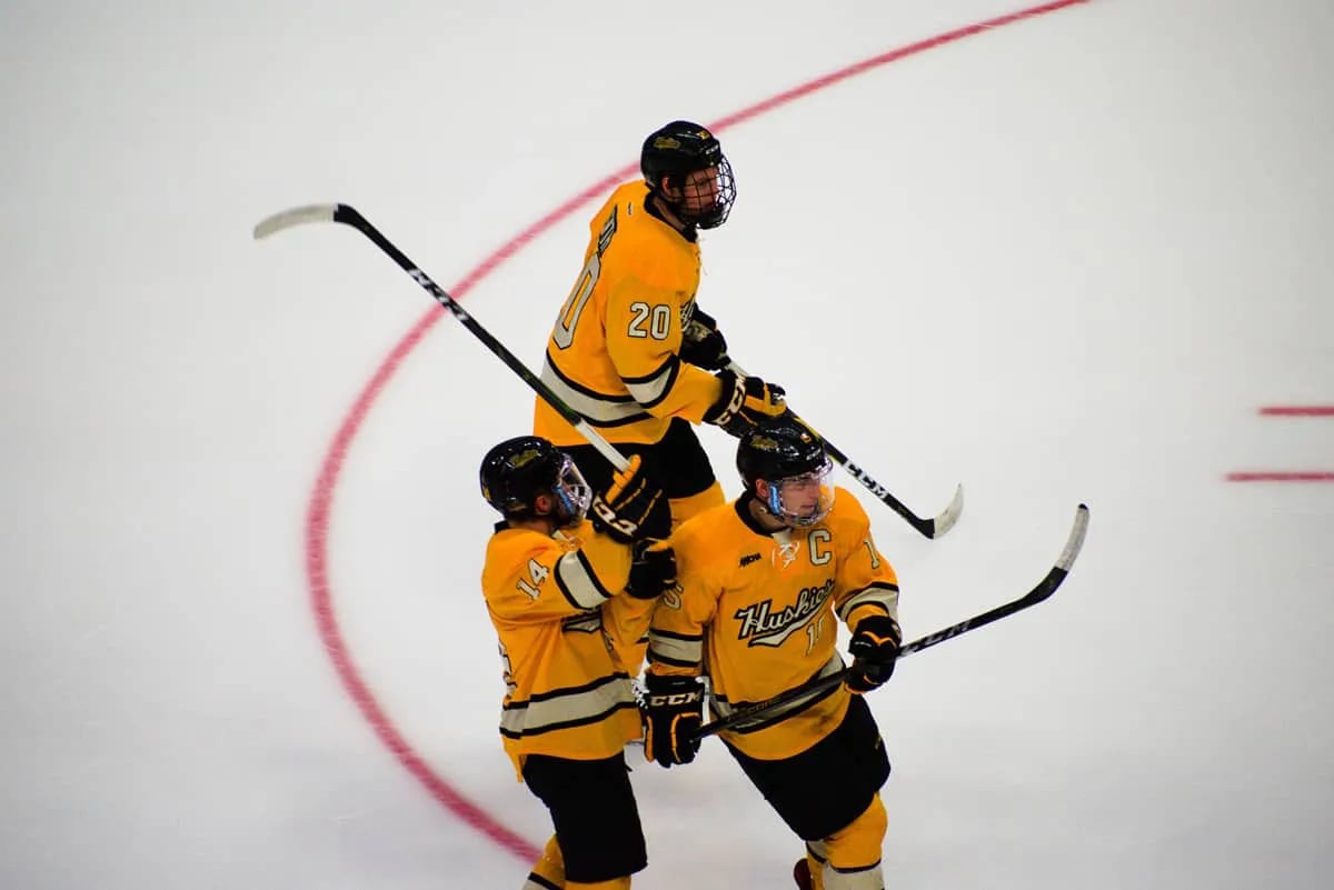 Three hockey player teammates in yellow jerseys on ice.