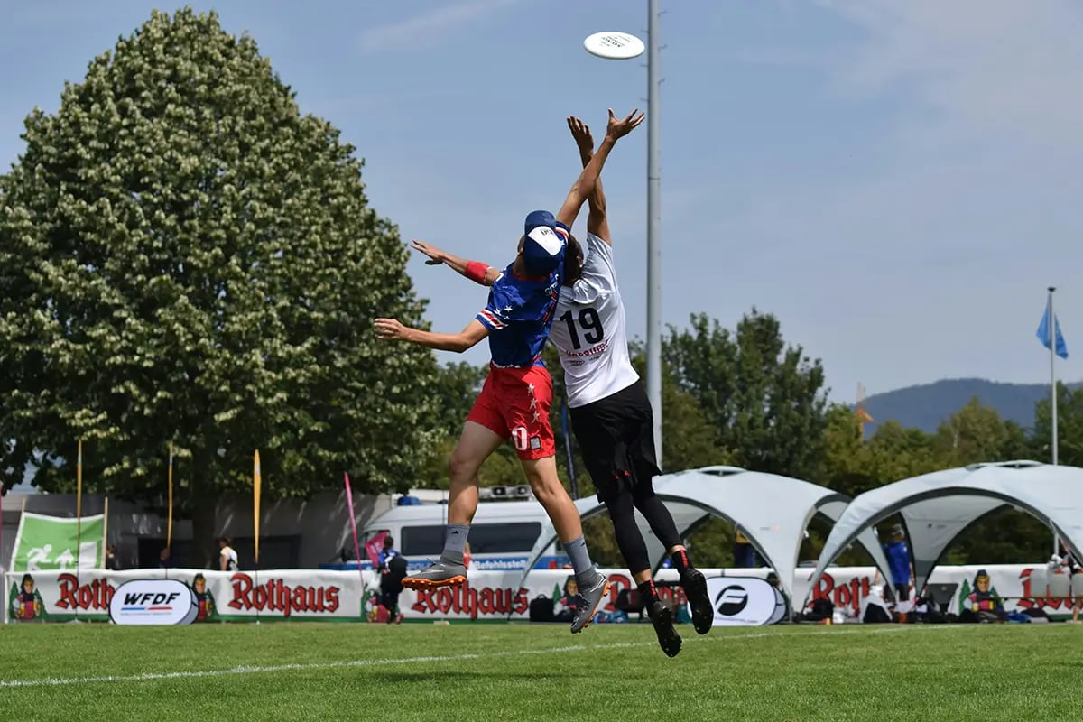 two men playing ultimate both reaching for frisbee in air
