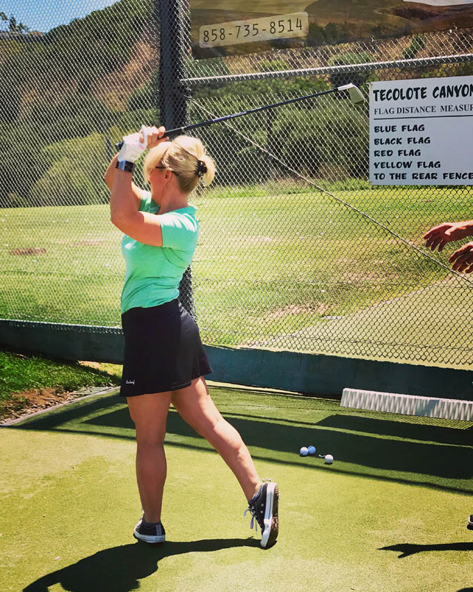 woman swinging golf club at driving range