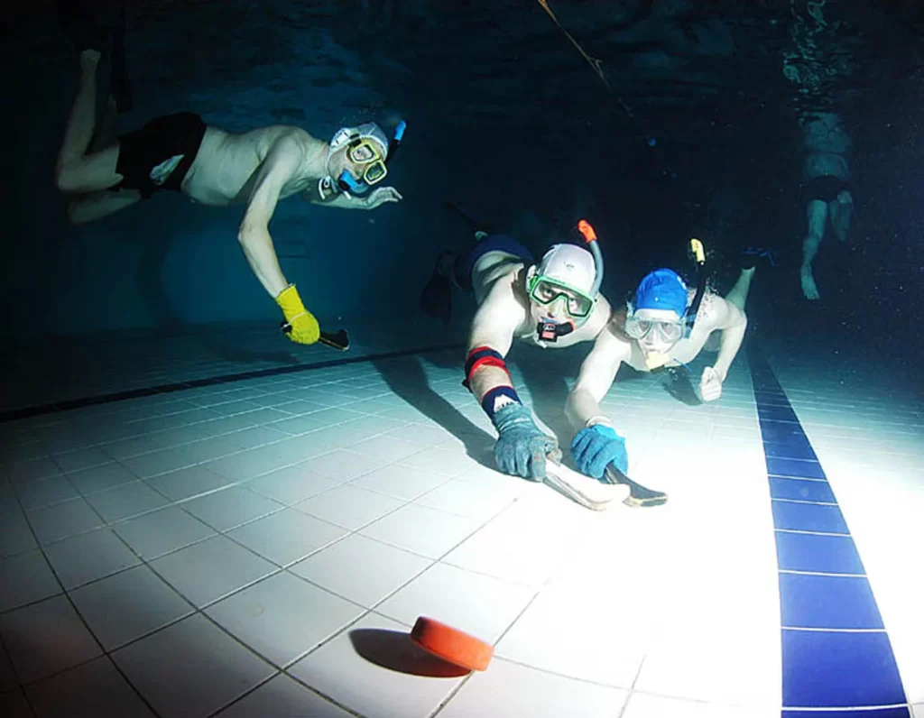 Three men at bottom of pool playing game of Octopush