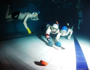 Three men at bottom of pool playing non-mainstream sport of