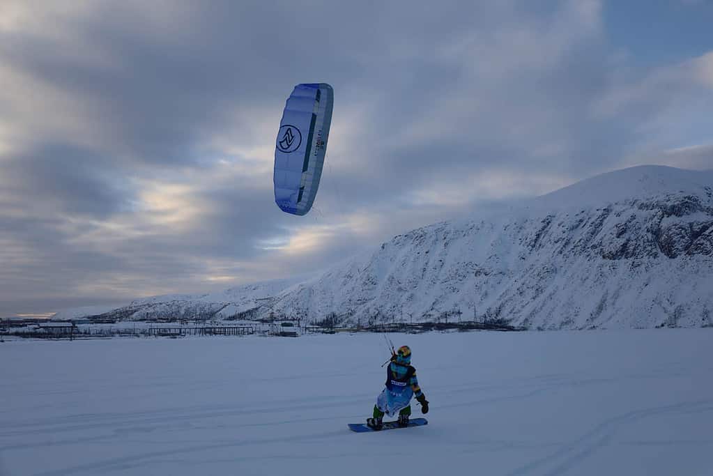 snowkiter surrounded by snow and mountains with cloudy sky
