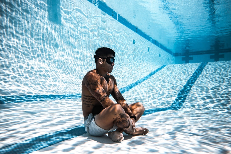 man sitting at bottom of pool holding his breath
