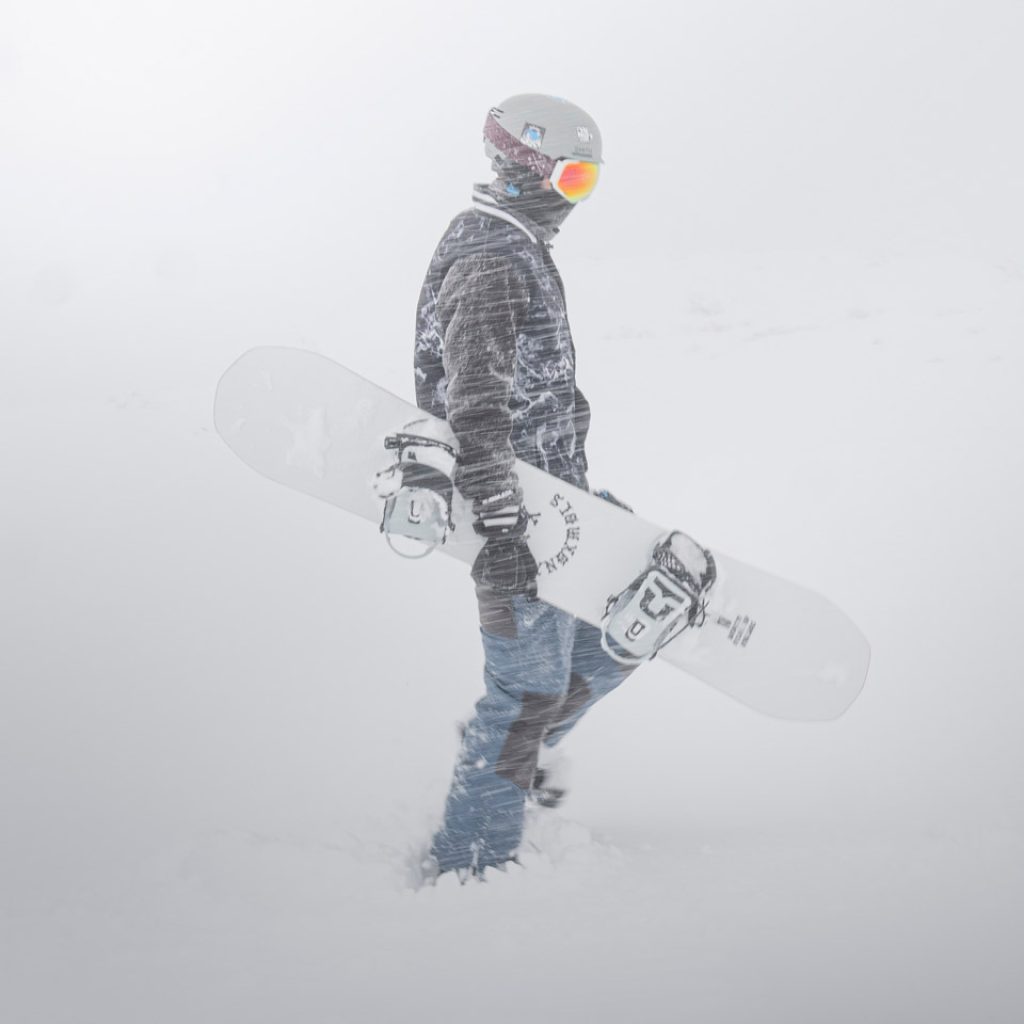 Lone snowboarder in powdery snow holding snowboard under arm