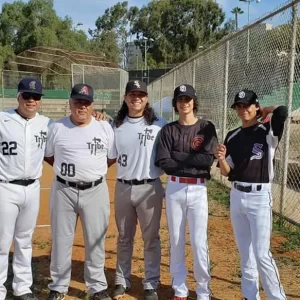 Three generations of Carrillo men in baseball uniforms posing together on baseball field.