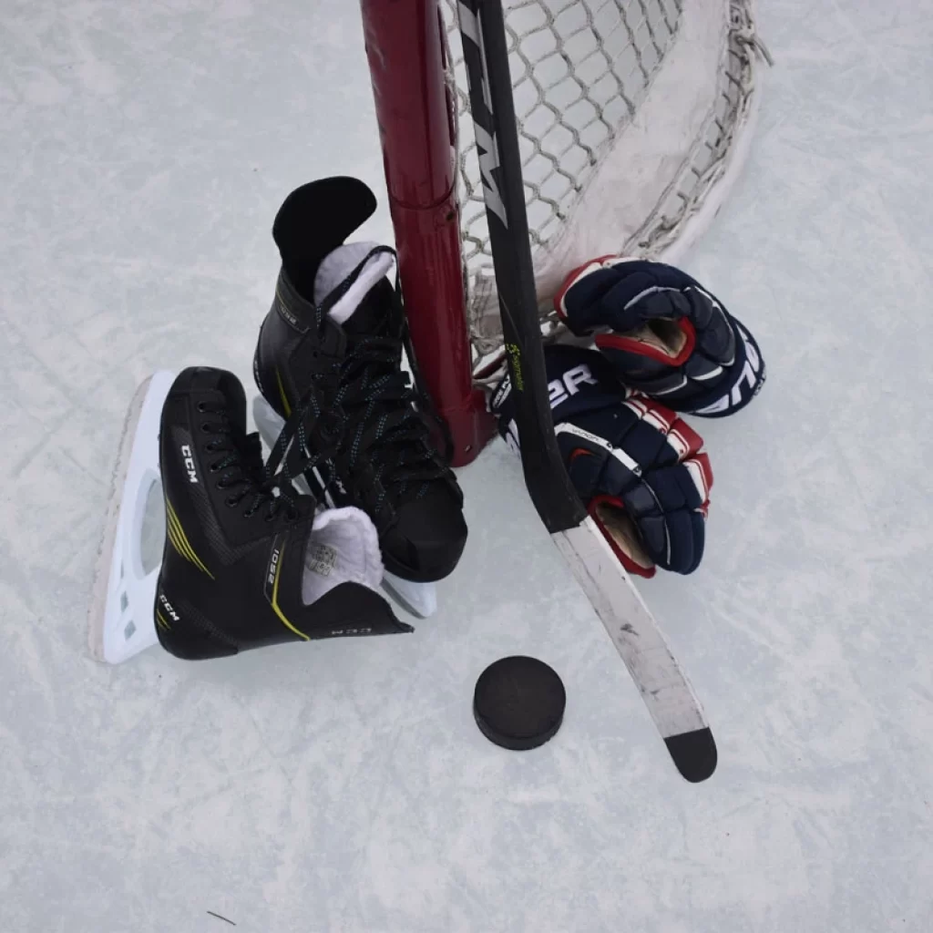 Hockey skates, glvoes, puck and stick lying on ie near goal post
