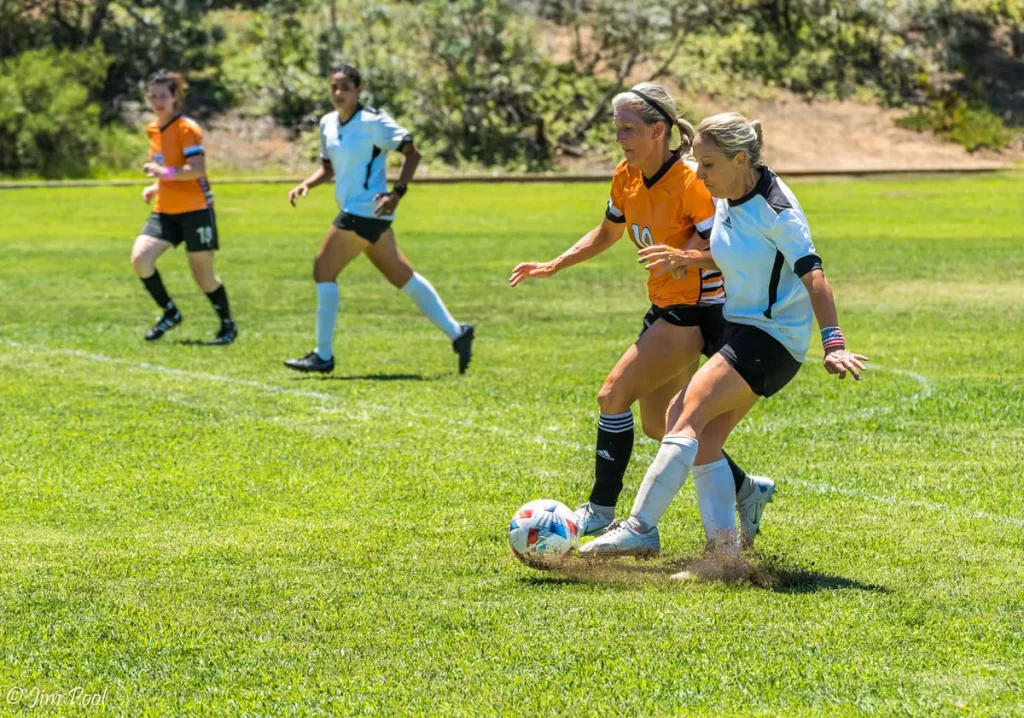 Two women on soccer field battling for the soccer ball showing high calorie burn sport