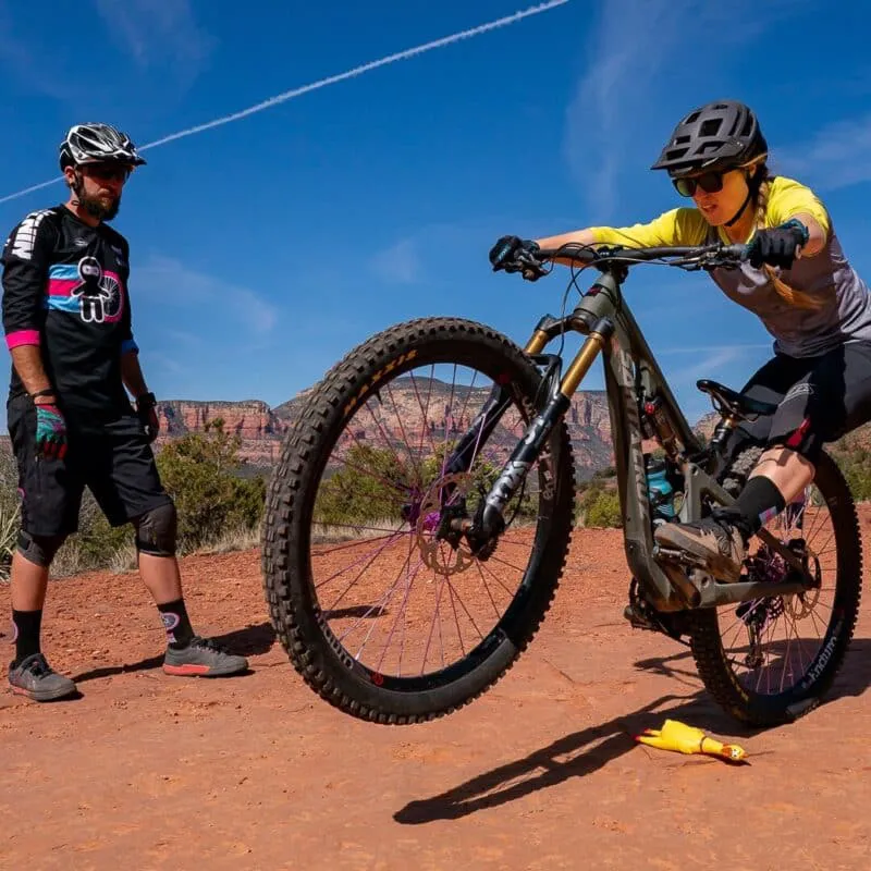 woman popping wheelie on moutain bike as instructor looks on