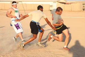 three men playing flag football on sand