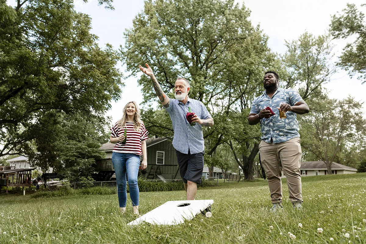 three friends playing cornhole in a grassy field