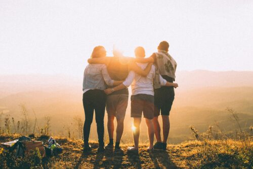 four hikers on top of a mountain looking down with arms interlocked