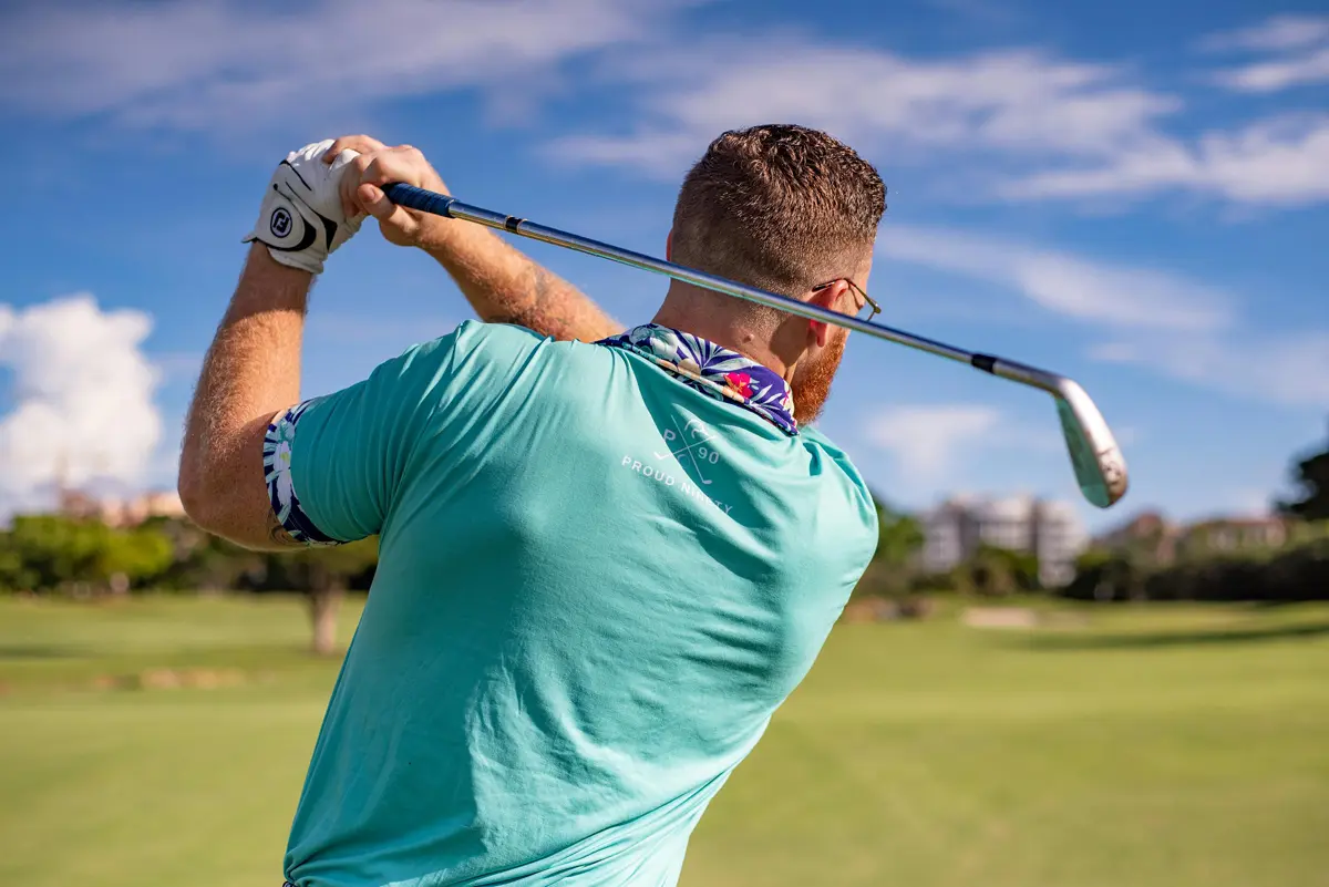 man in blue shirt after completing a golf swing shown from behind