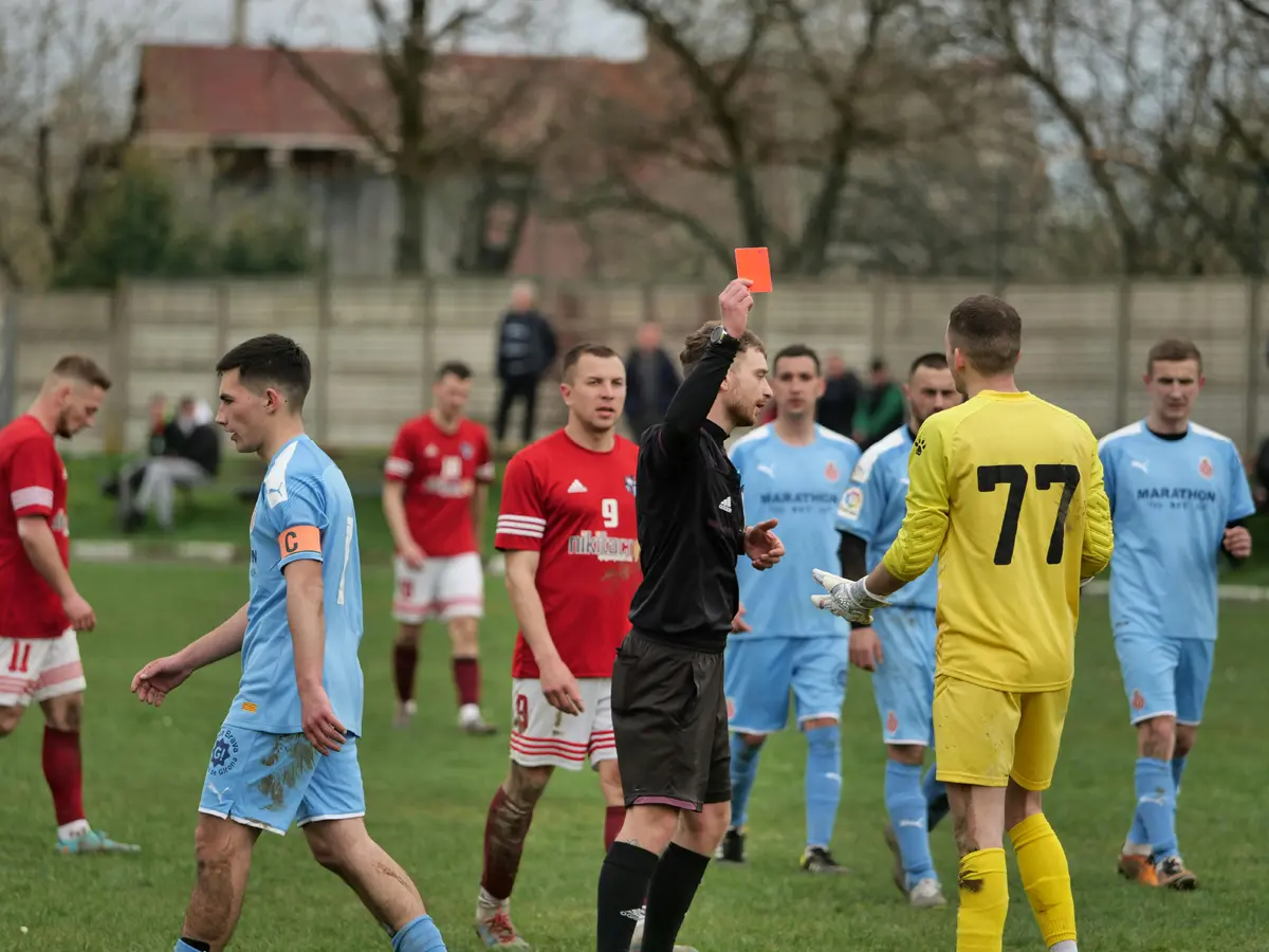 two soccer teams surrounding ref holding red card