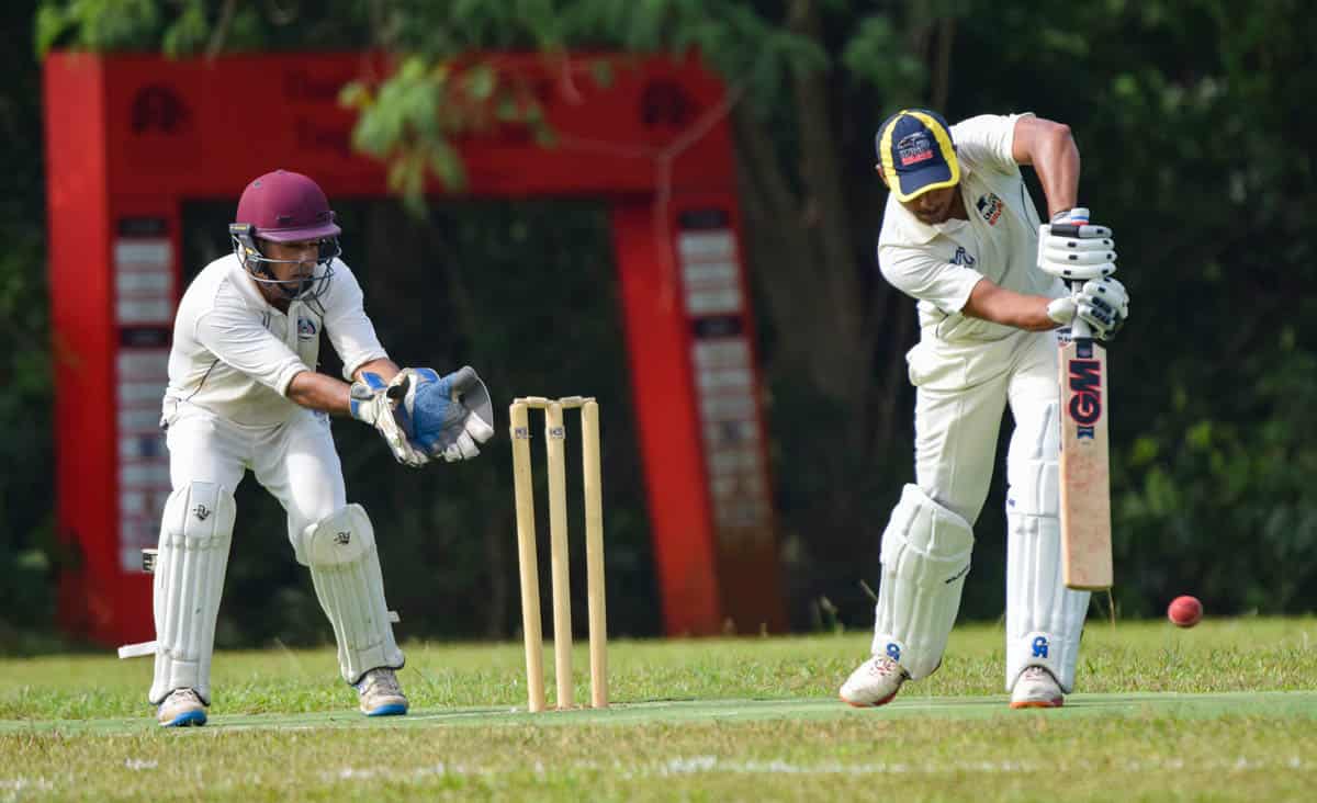 Two men playing cricket with one hitting and and behind him catching.