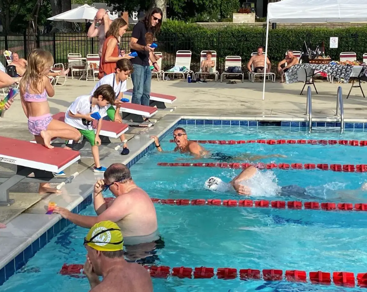 Adults in pol with kids hanging out on the platforms on edge of pool
