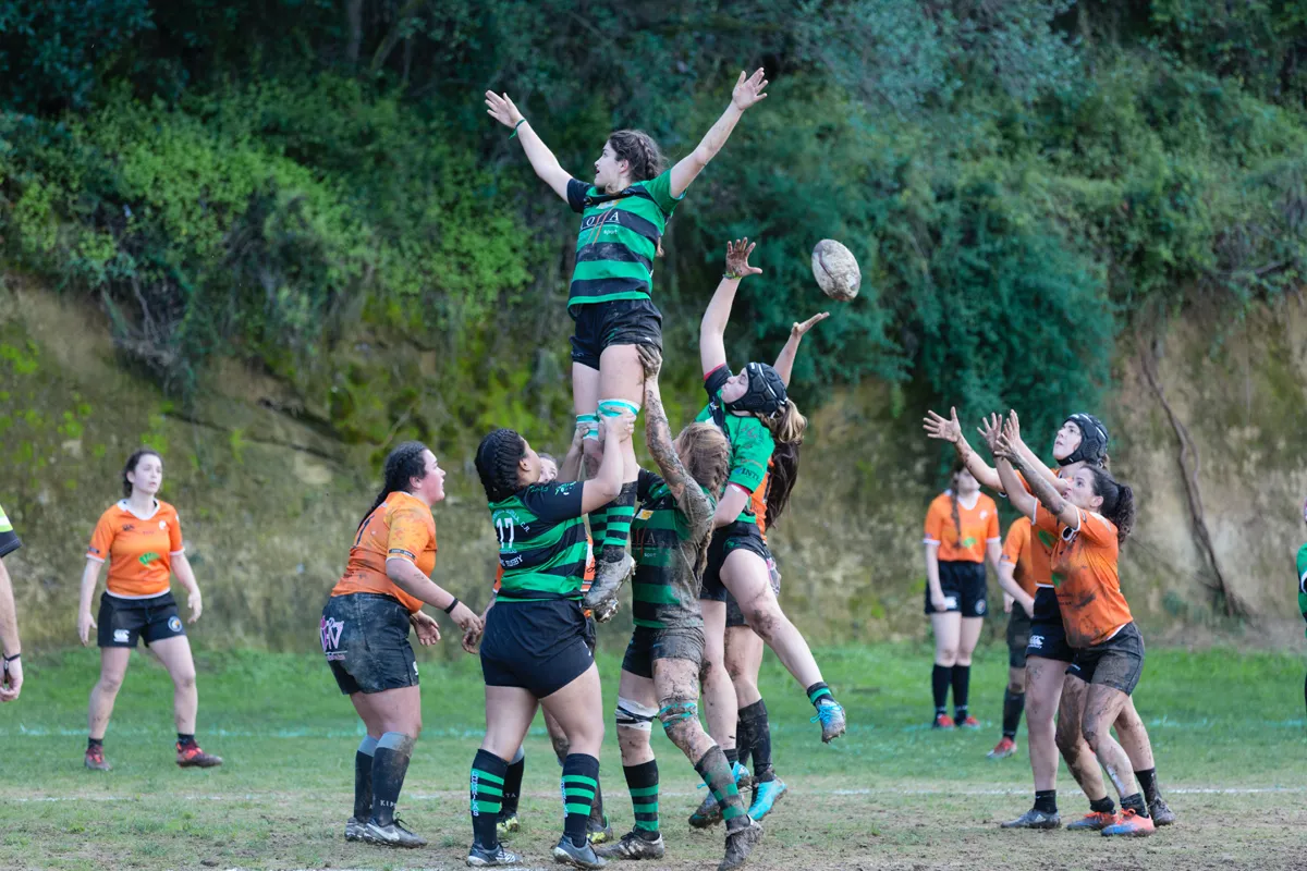 Female rugby players from opposing teams, with one team in a lift formation and a couple players reaching for ball