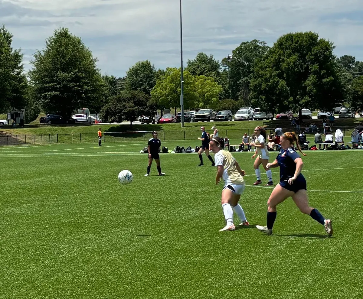 two women's soccer players from opposing teams goin after ball